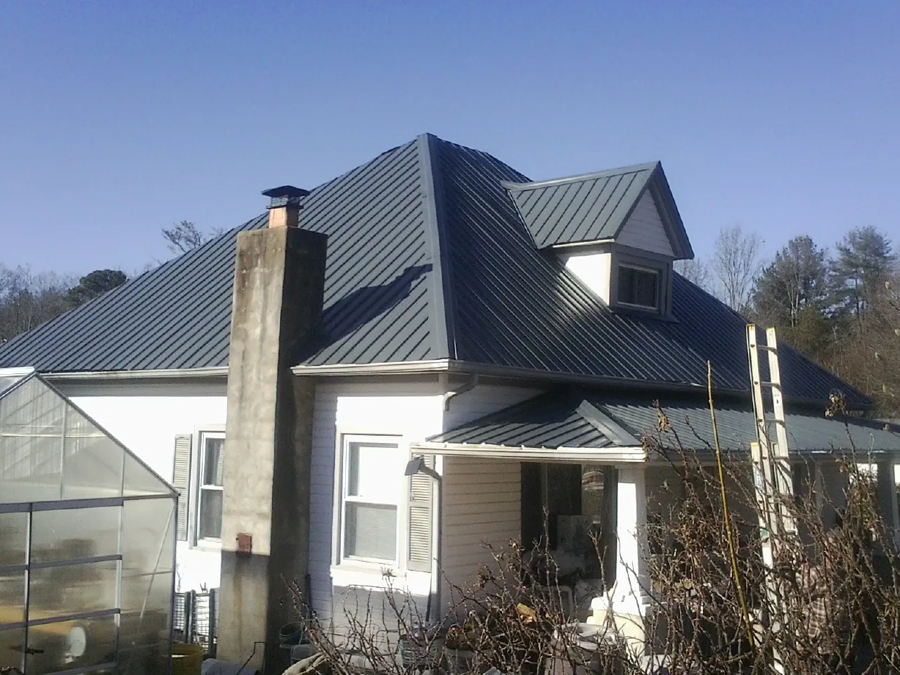 Dark blue standing seam metal roof on a white farmhouse with dormer — Slate & Tile Roof Repair by Roofing Brothers in Crowley