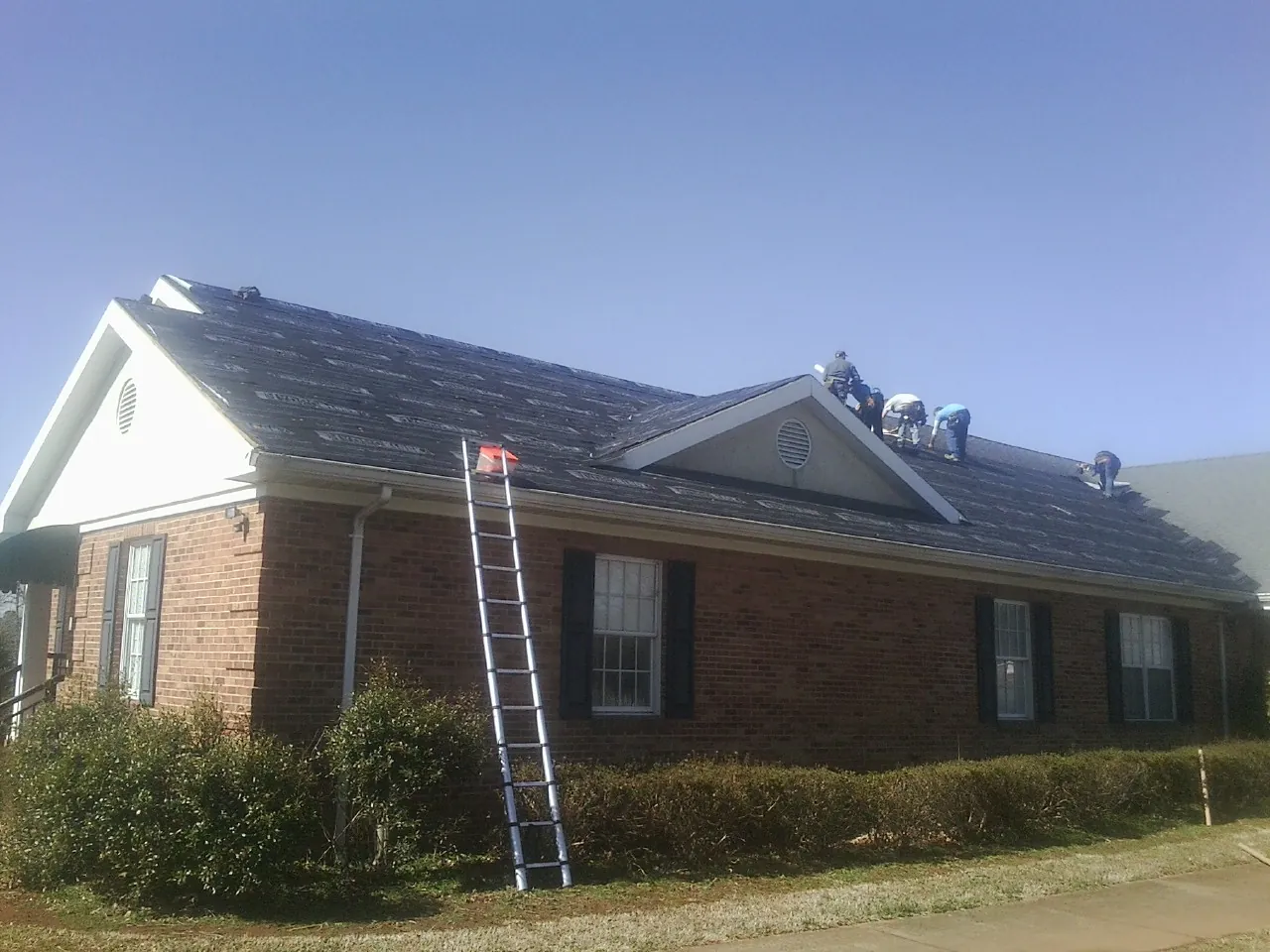 Crew tearing shingles off a brick ranch roof with a ladder set — Emergency Roof Repair work by our crew in Crowley