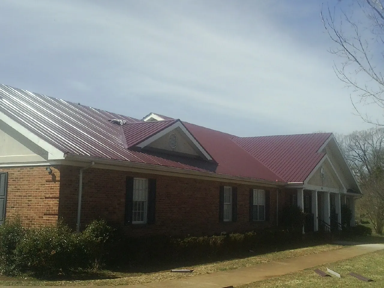 Red metal roof with gabled entries on a long brick building, from a Hail Damage Roof Repair job in Crowley