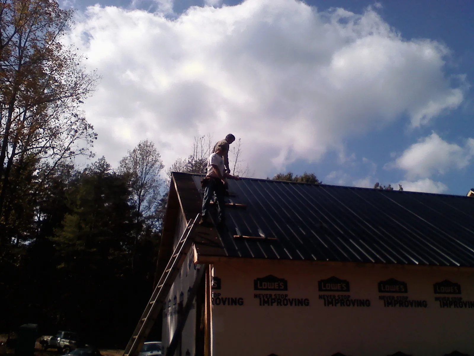 Roofer fastening dark metal panels high against a cloudy sky, from a Roof Inspection job in Crowley