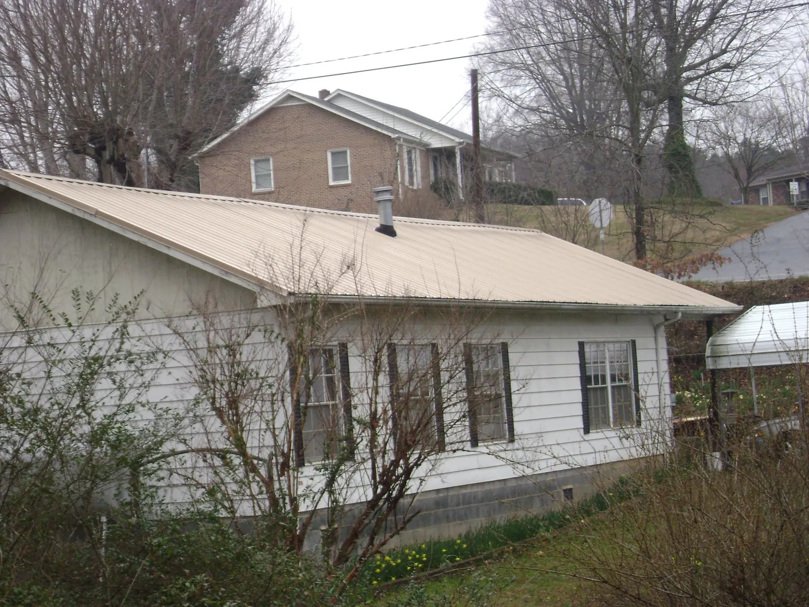 Tan metal roof on a white sided house set into a hillside — Commercial Roofing by Roofing Brothers in Crowley